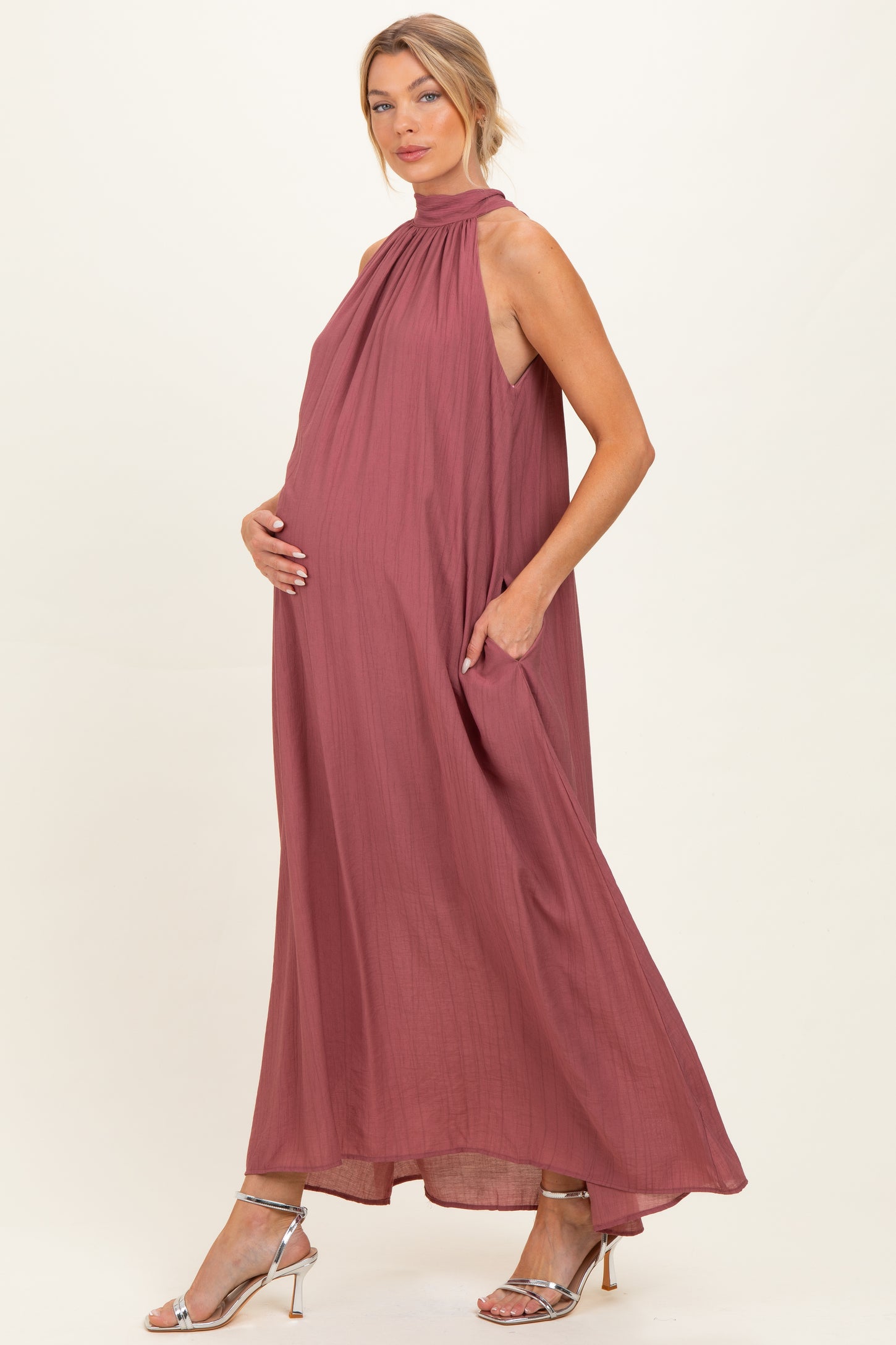 woman wearing a dusty rose sleeveless maternity dress with a high neck and pockets, showcasing her baby bump