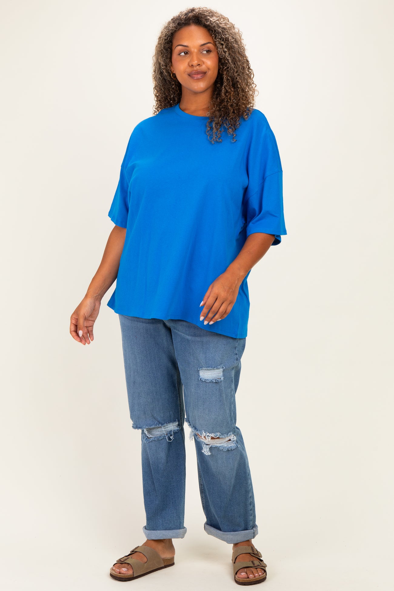 woman wearing an oversized bright blue t-shirt and distressed light wash jeans with open-toe sandals