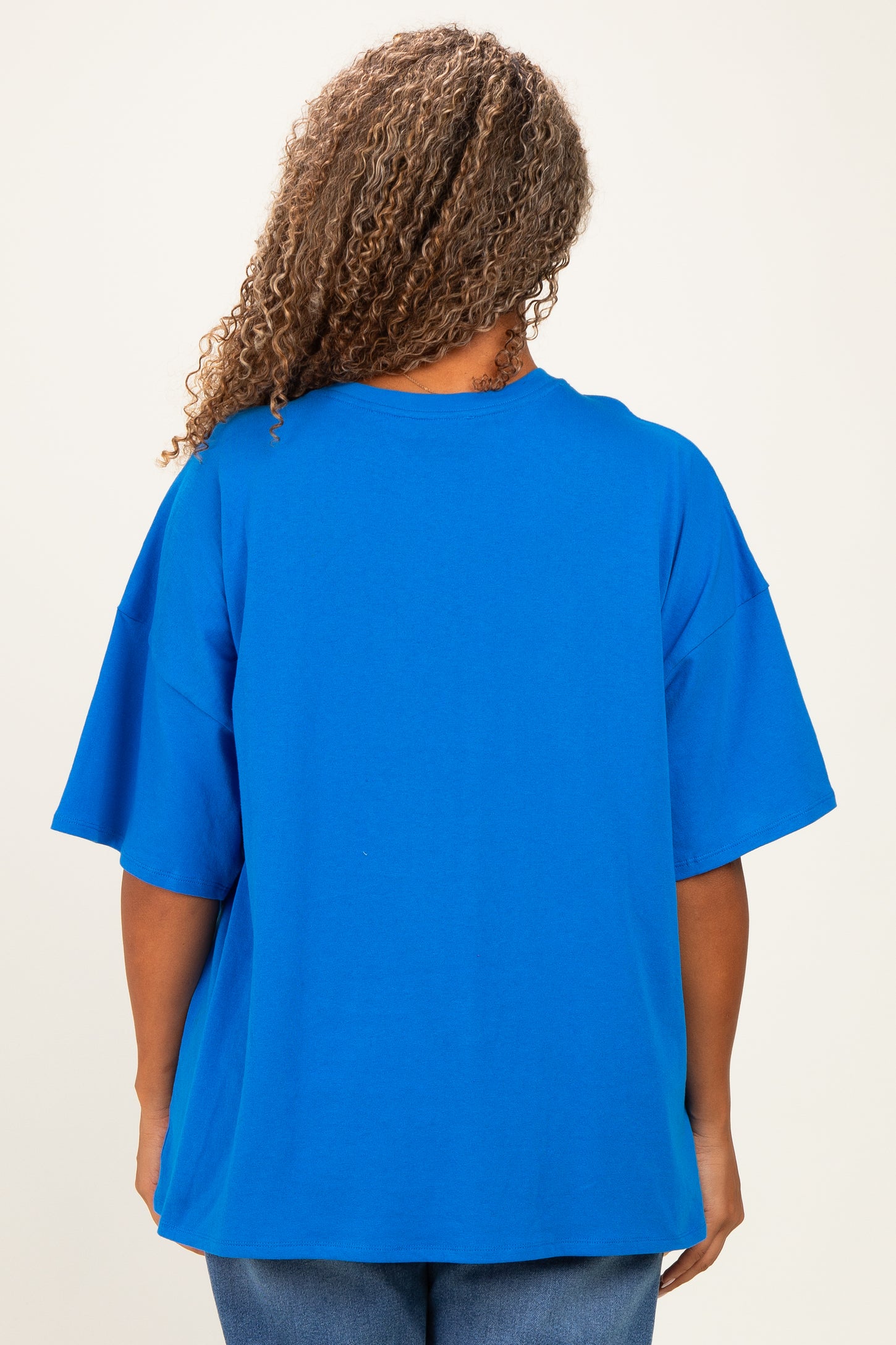 plus size woman wearing a bright blue oversized t-shirt, view from the back, with curly hair