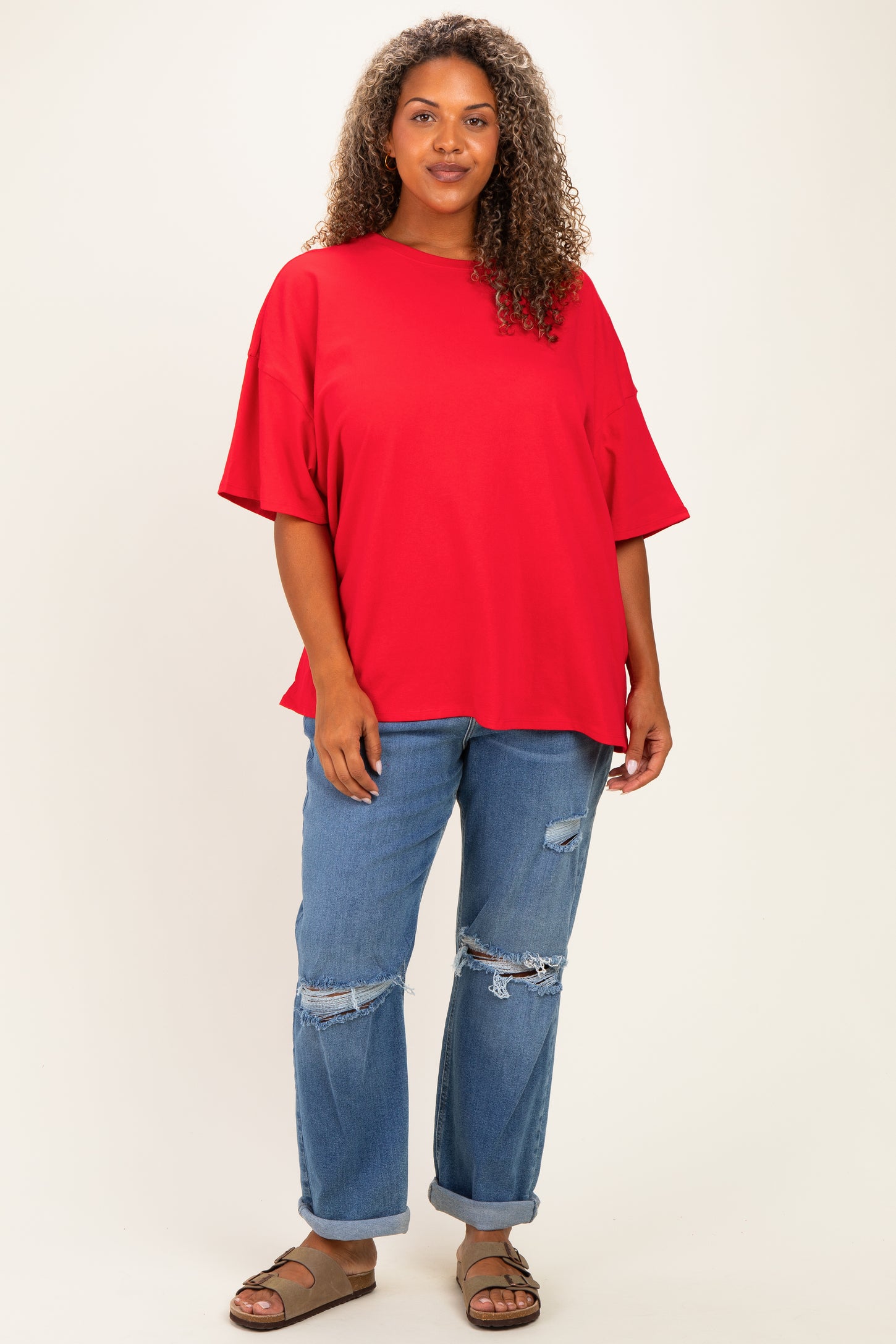 woman wearing a bright red oversized t-shirt and distressed blue jeans with brown sandals