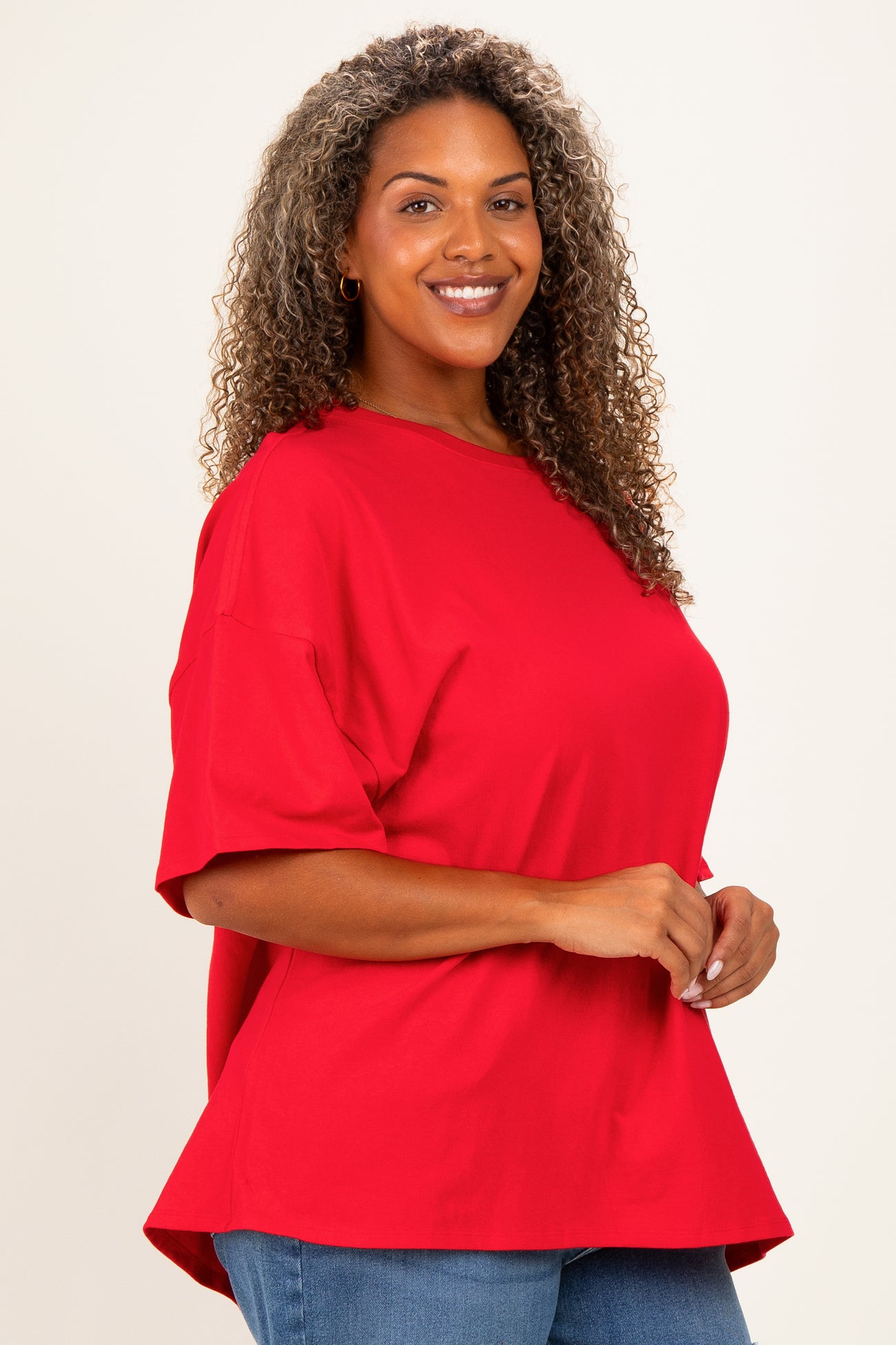 woman wearing a red oversized t-shirt with a curved hem and smiling while posing to the side