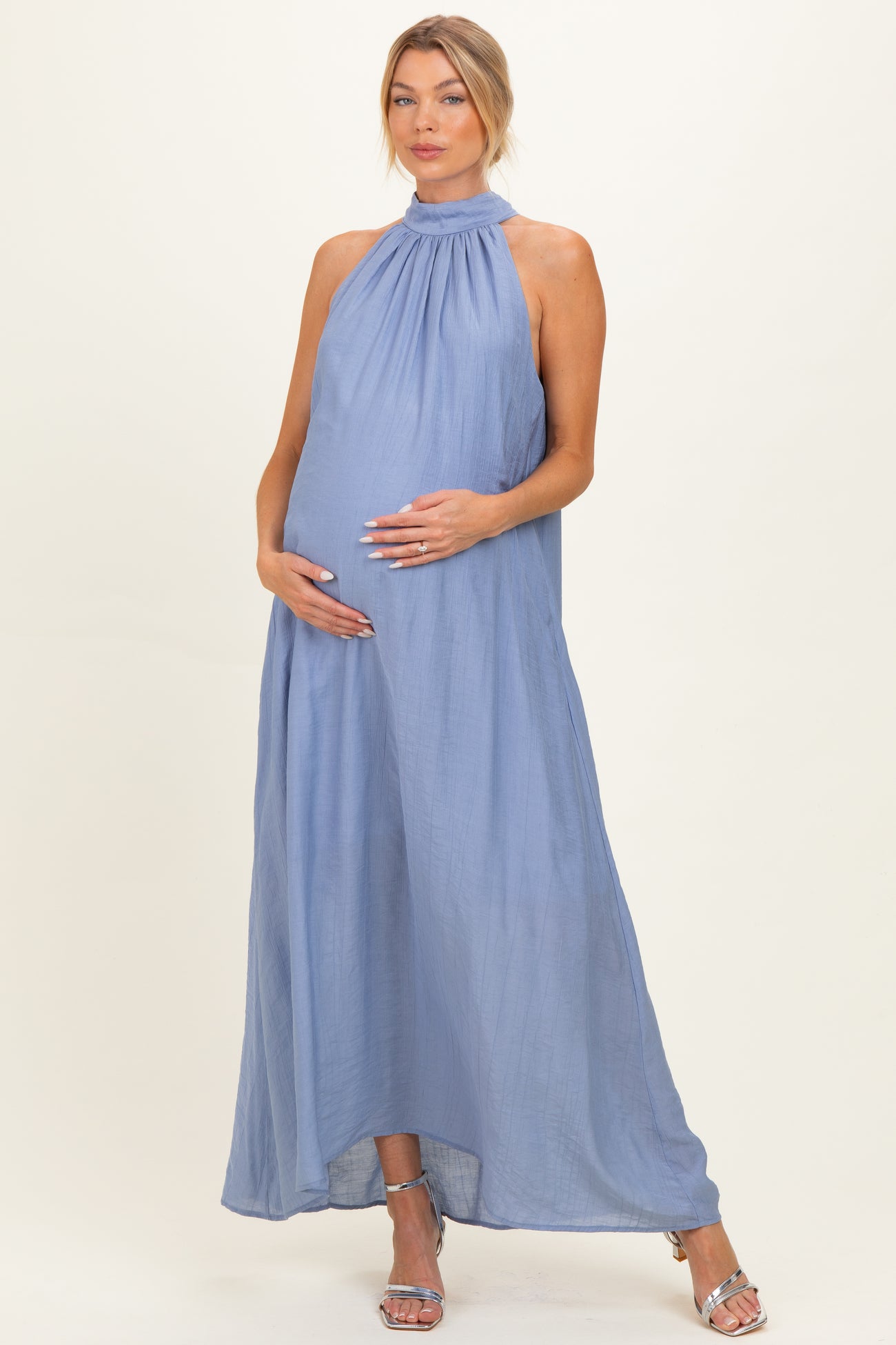 woman wearing a light blue halter neck maternity dress, standing and cradling her baby bump