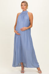 woman wearing a light blue halter neck maternity dress, standing and cradling her baby bump
