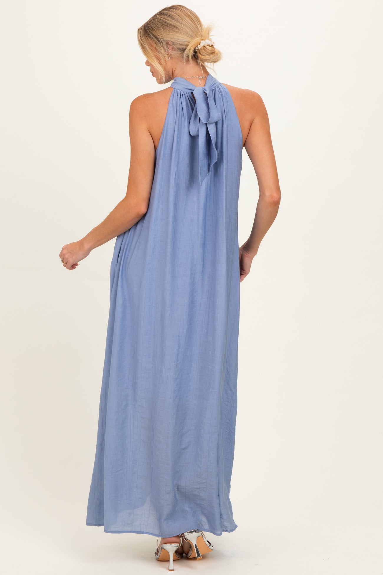 woman wearing a light blue sleeveless maternity maxi dress with a bow tie detail at the back