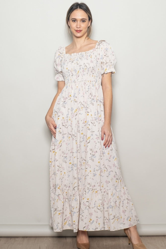 woman wearing a long floral maxi dress with puff sleeves and a square neckline, smiling against a neutral background