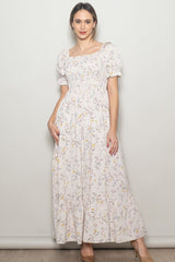 woman wearing a long floral maxi dress with puff sleeves and a square neckline, smiling against a neutral background