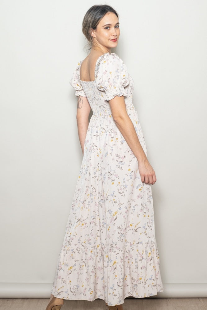 woman wearing a floral maxi dress with puff sleeves and a fitted bodice, posing from the back against a neutral background