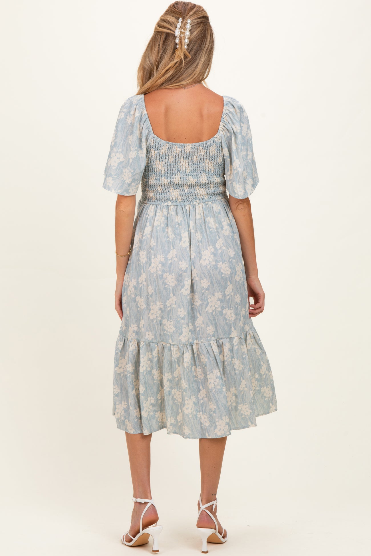 woman wearing a light blue floral maternity dress with a smocked bodice and tiered skirt, shown from the back