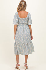 woman wearing a light blue floral maternity dress with a smocked bodice and tiered skirt, shown from the back