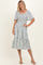 woman wearing a light blue floral midi dress with smocked bodice and flutter sleeves, standing with one hand on her hip