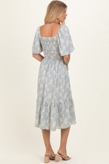 woman wearing a light blue floral midi dress with a smocked bodice and puff sleeves, shown from the back