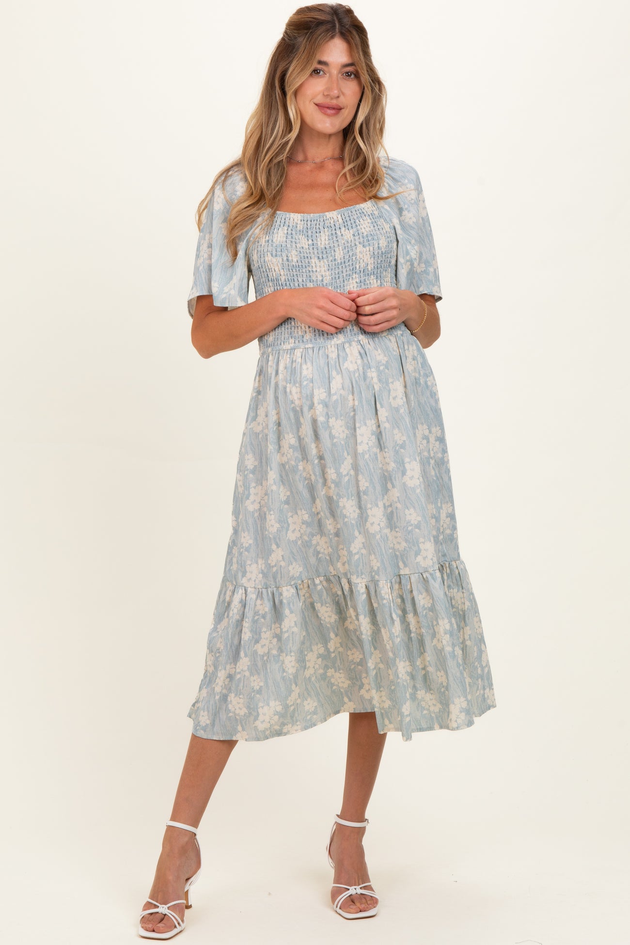 woman wearing a light blue floral maternity dress with short puff sleeves and a tiered skirt, baby bump visible