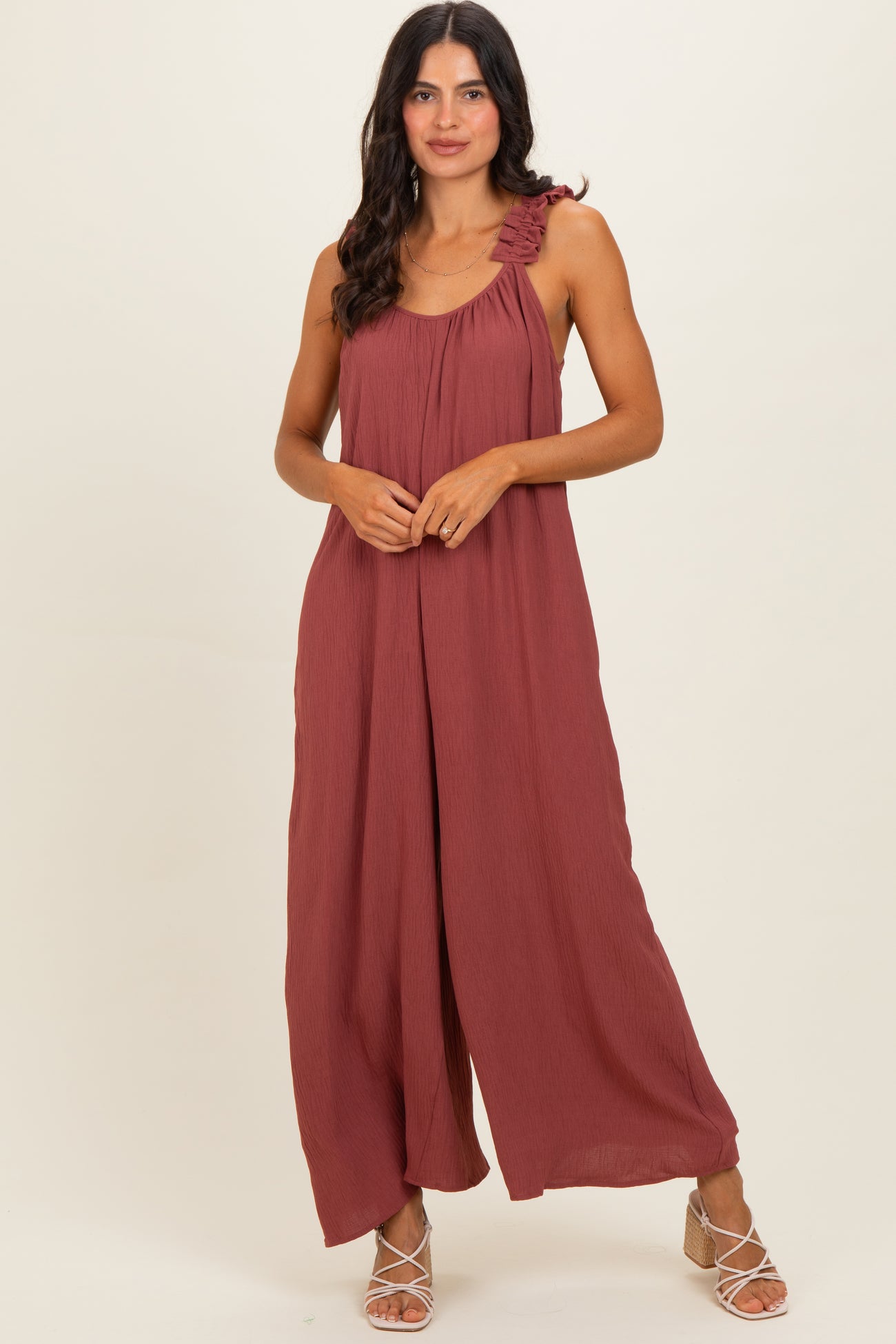 woman wearing a rust-colored sleeveless maxi dress with ruffle shoulders and wide-leg style