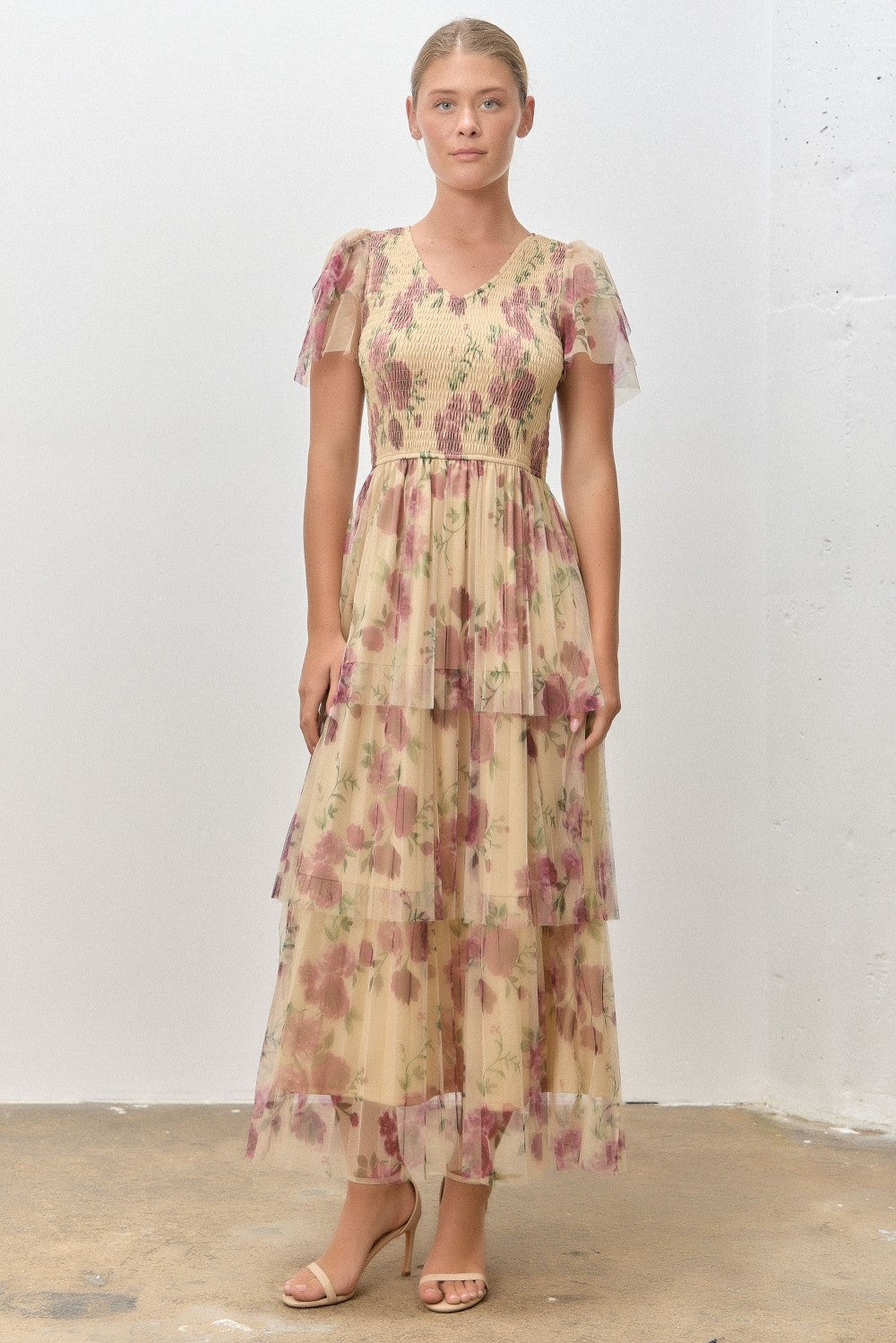 woman wearing a floral tiered maxi dress with short puff sleeves in shades of beige and pink.