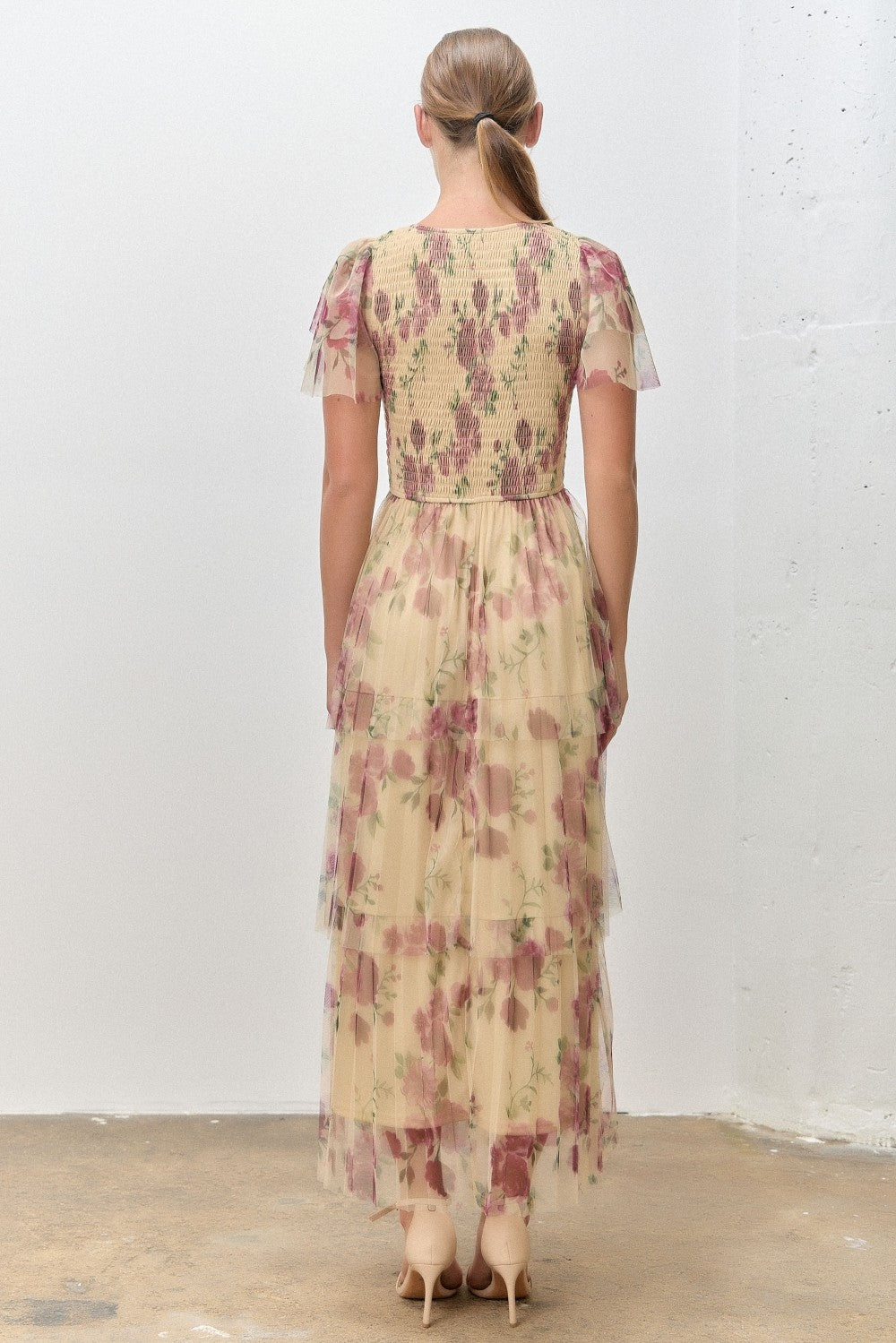 woman wearing a yellow floral maxi dress with tiered ruffles, showcasing a fitted bodice and flutter sleeves from the back