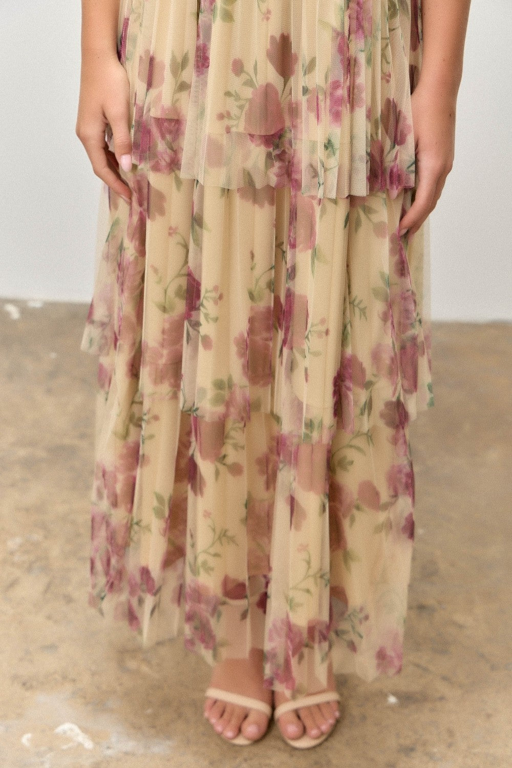 woman wearing a floral print sheer maxi dress with layered designs and a beige background, paired with light sandals