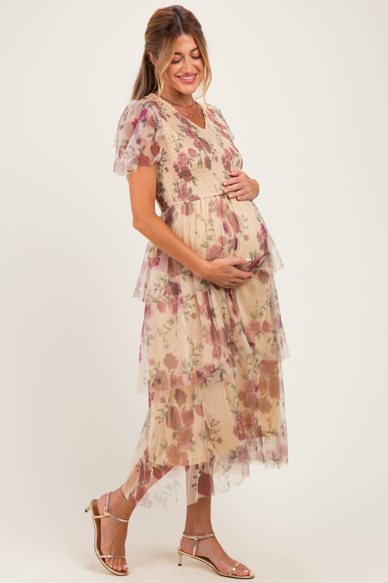 woman wearing a floral tiered maternity dress with a v-neckline, gently holding her baby bump