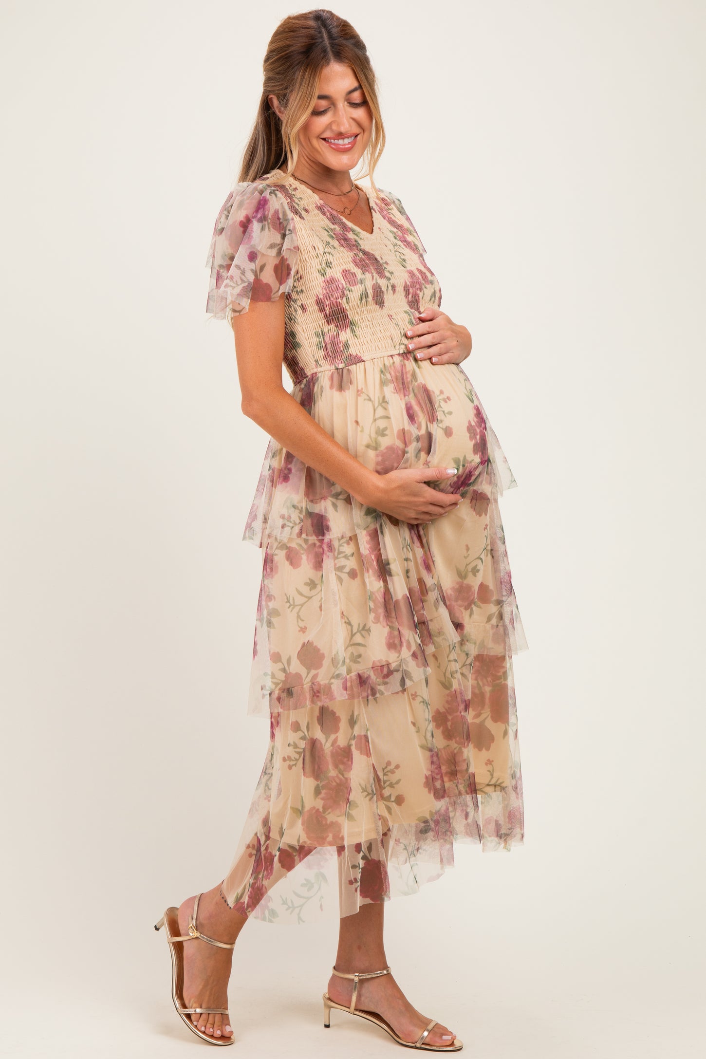 woman wearing a floral tiered maternity dress with a v-neckline, gently holding her baby bump