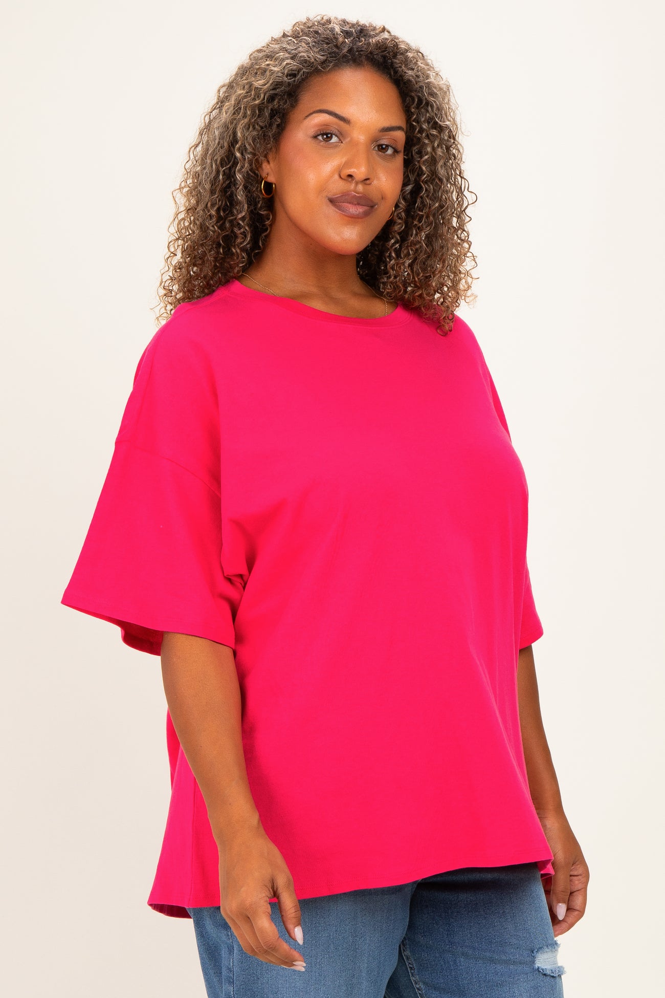 woman wearing a bright pink oversized t-shirt with short sleeves and a relaxed fit, paired with blue jeans