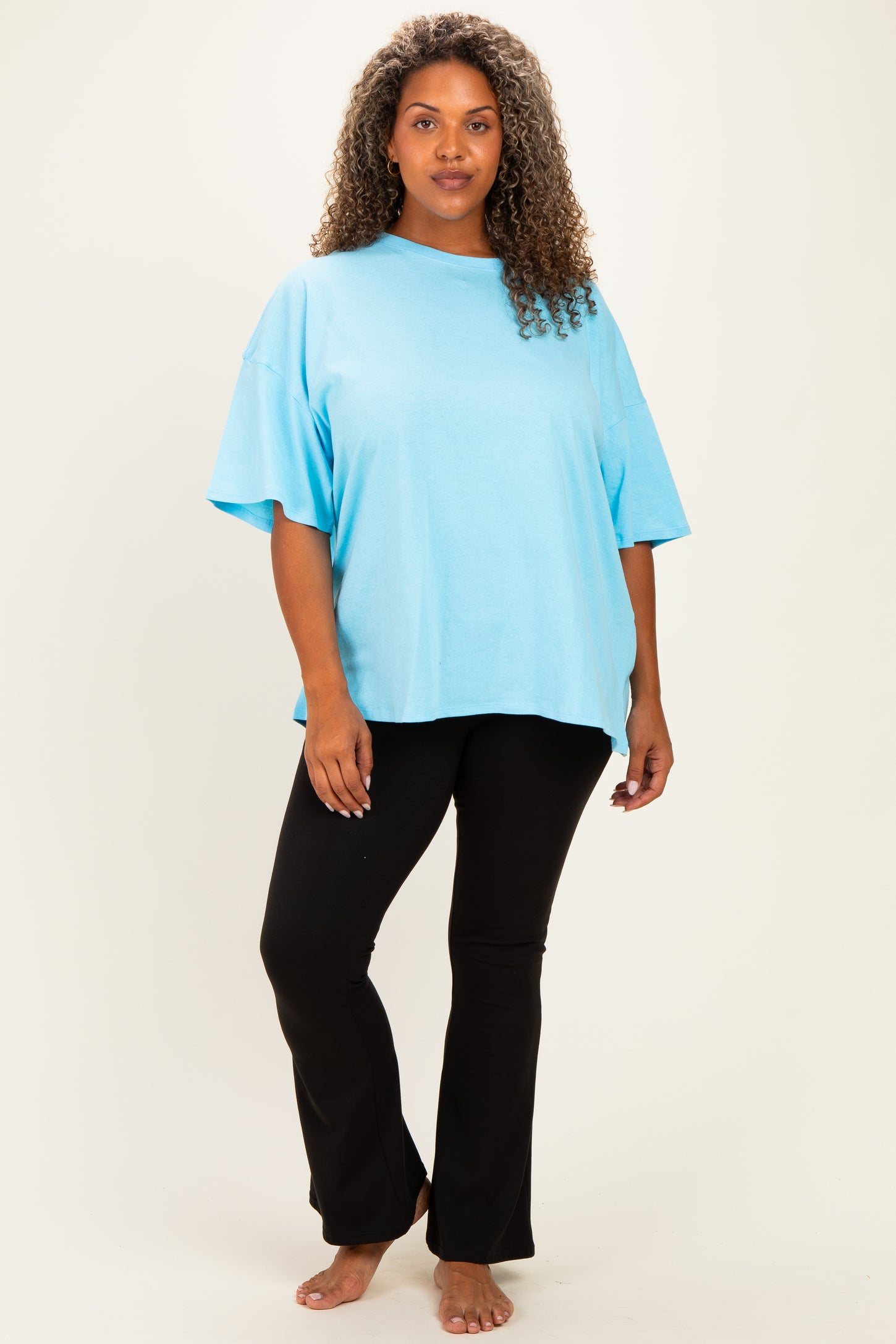 woman wearing a light blue oversized t-shirt and black flared pants, standing barefoot against a neutral background