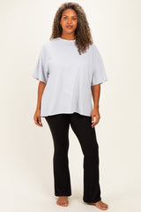 woman wearing a light gray oversized t-shirt and black flared pants, standing barefoot against a neutral background