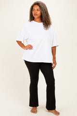woman wearing a white oversized t-shirt and black flared pants, standing barefoot against a light background