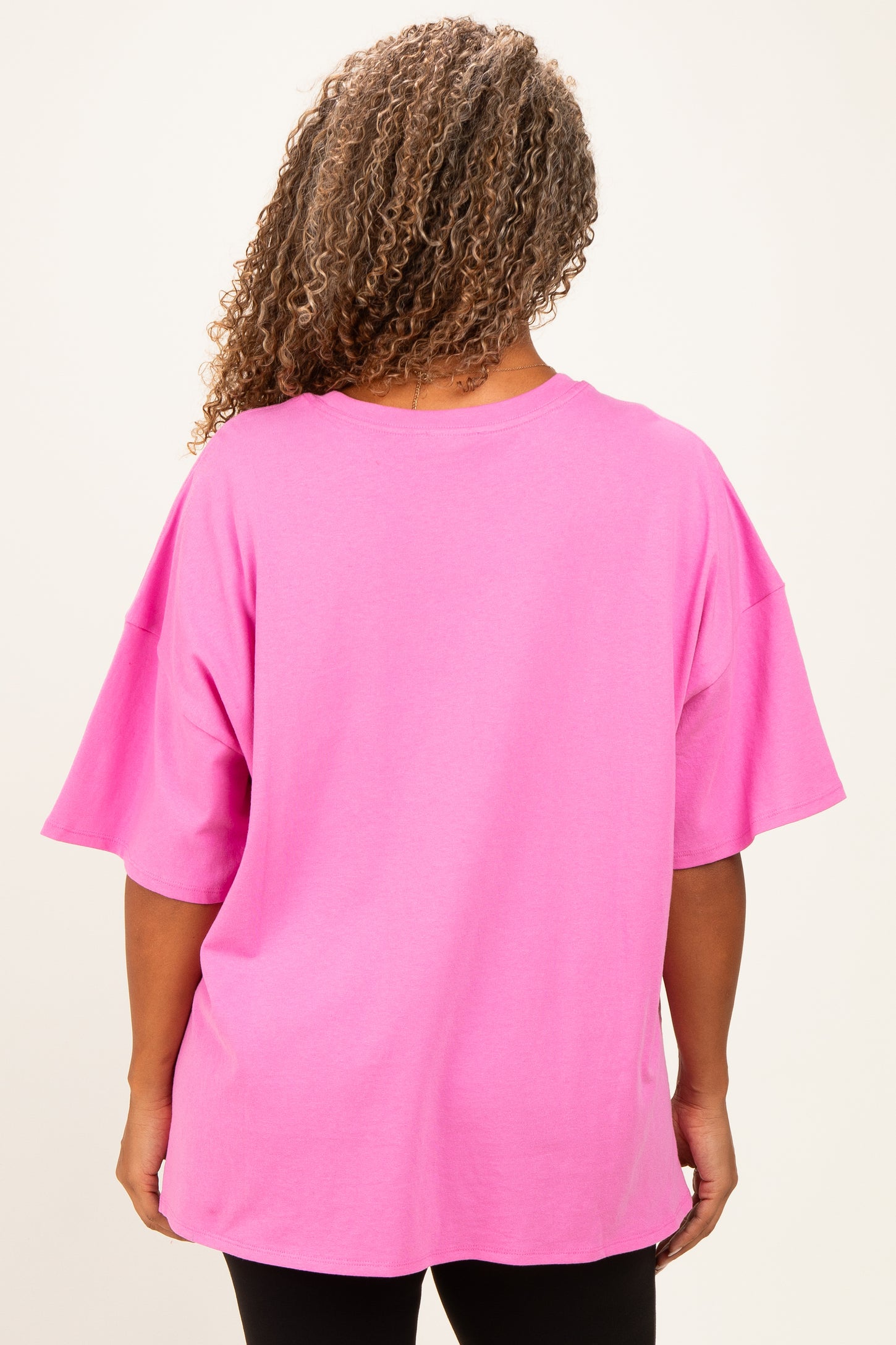 woman wearing a bright pink oversized t-shirt, viewed from the back, with short sleeves and relaxed fit