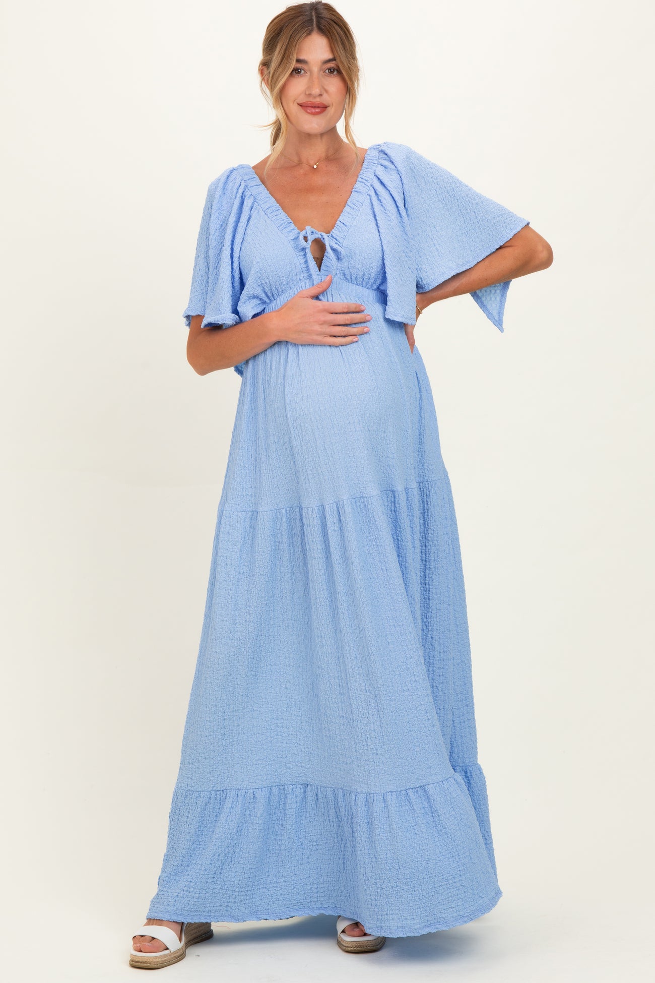 woman wearing a light blue maternity maxi dress with flutter sleeves and a tie detail, holding her baby bump