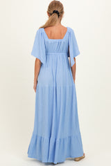 woman wearing a back view of a light blue maternity maxi dress with flutter sleeves and tiered skirt