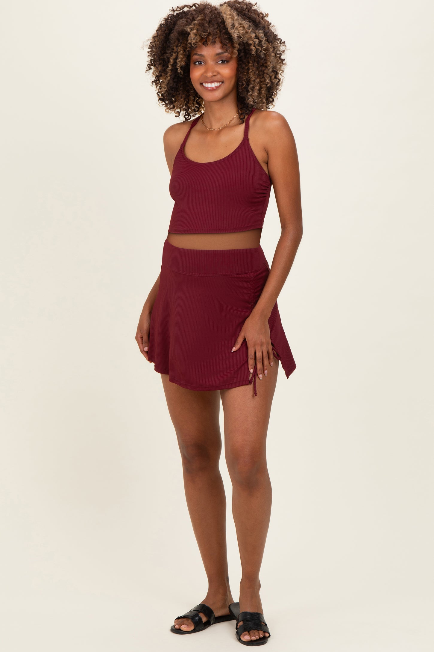 woman wearing a burgundy maternity crop top and matching skirt with a sporty style, no visible baby bump
