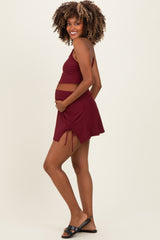 woman wearing a burgundy maternity bikini with a ruched skirt and holding her baby bump