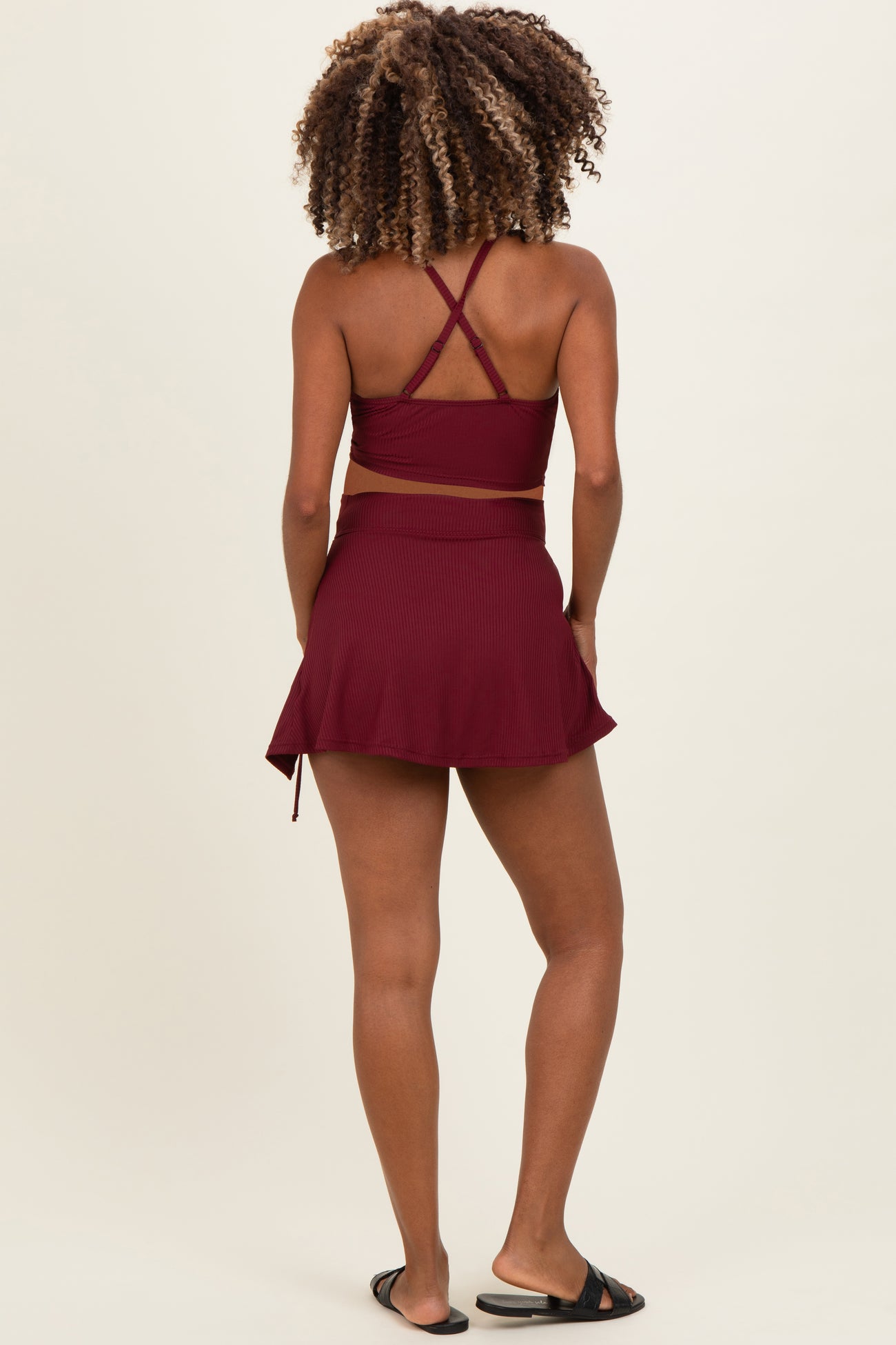 woman wearing a burgundy maternity swim top with cross-back straps and a matching skort, showing a baby bump