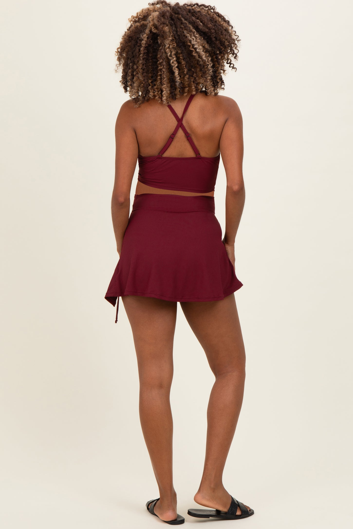 woman wearing a burgundy maternity swim top with cross-back straps and a matching skort, showing a baby bump