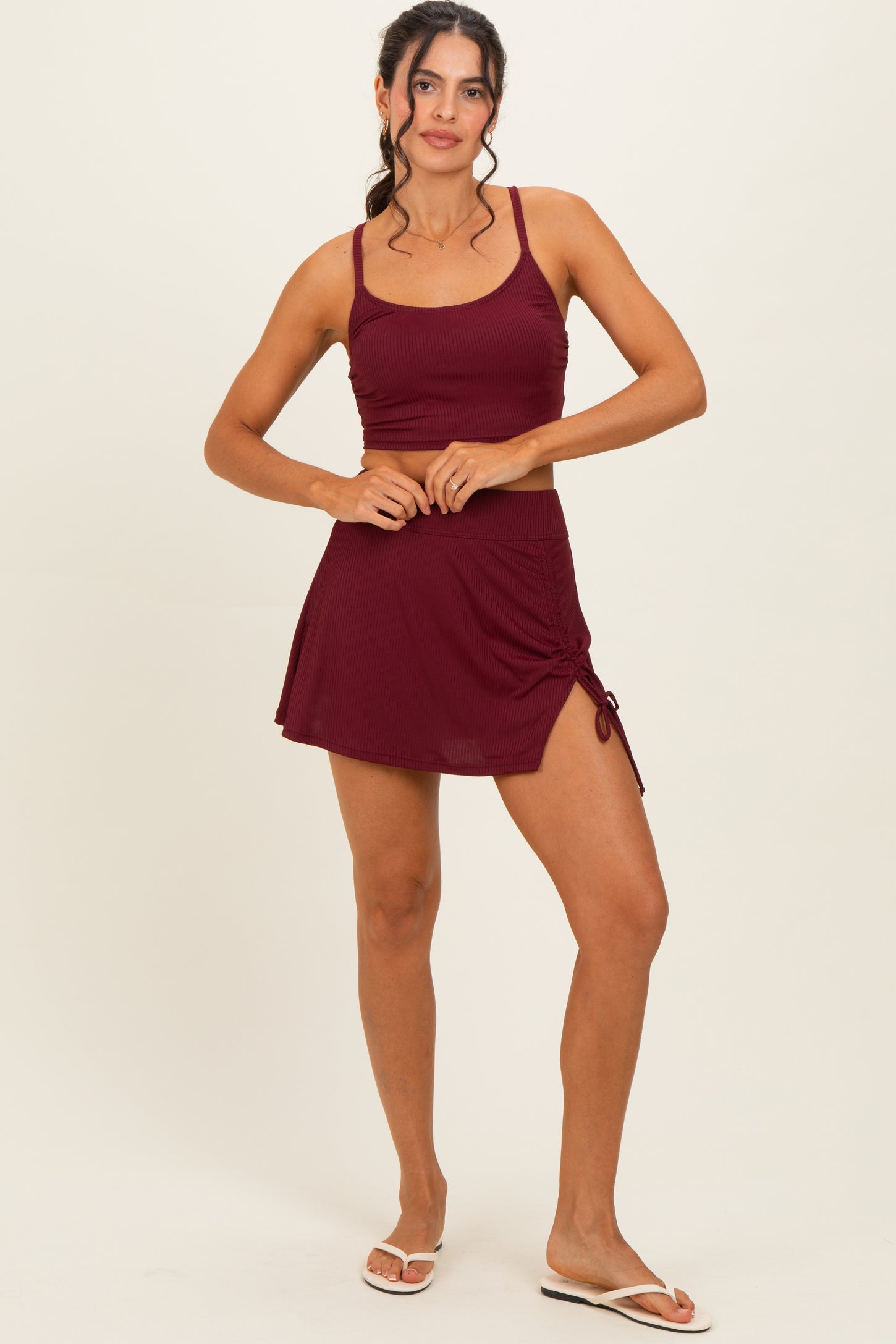 woman wearing a burgundy ribbed sports bra and matching short skirt with side drawstring details