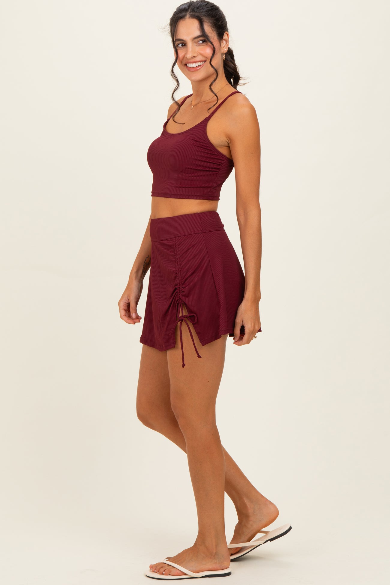 woman wearing a burgundy ribbed crop top and matching drawstring skort, styled with flip flops
