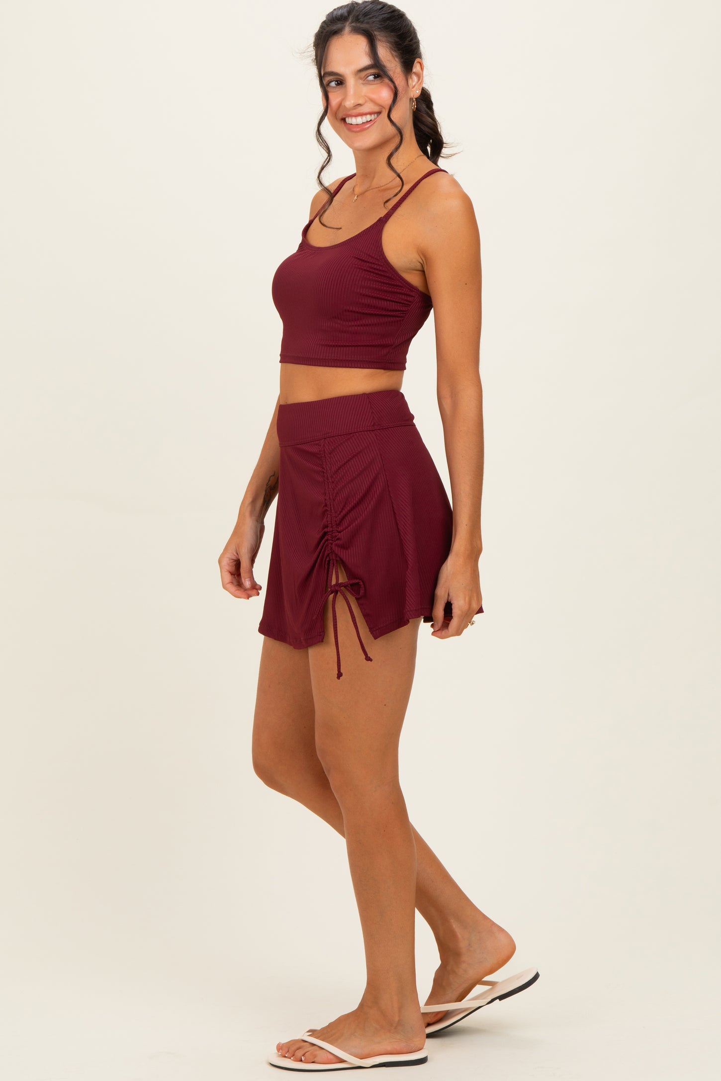 woman wearing a burgundy ribbed crop top and matching drawstring skort, styled with flip flops