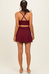 woman wearing a burgundy ribbed crop top with crisscross straps and a matching flared mini skirt