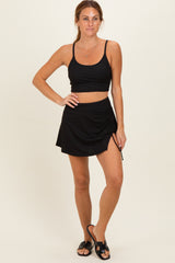 woman wearing a black ribbed crop top and matching skirt with a side tie detail