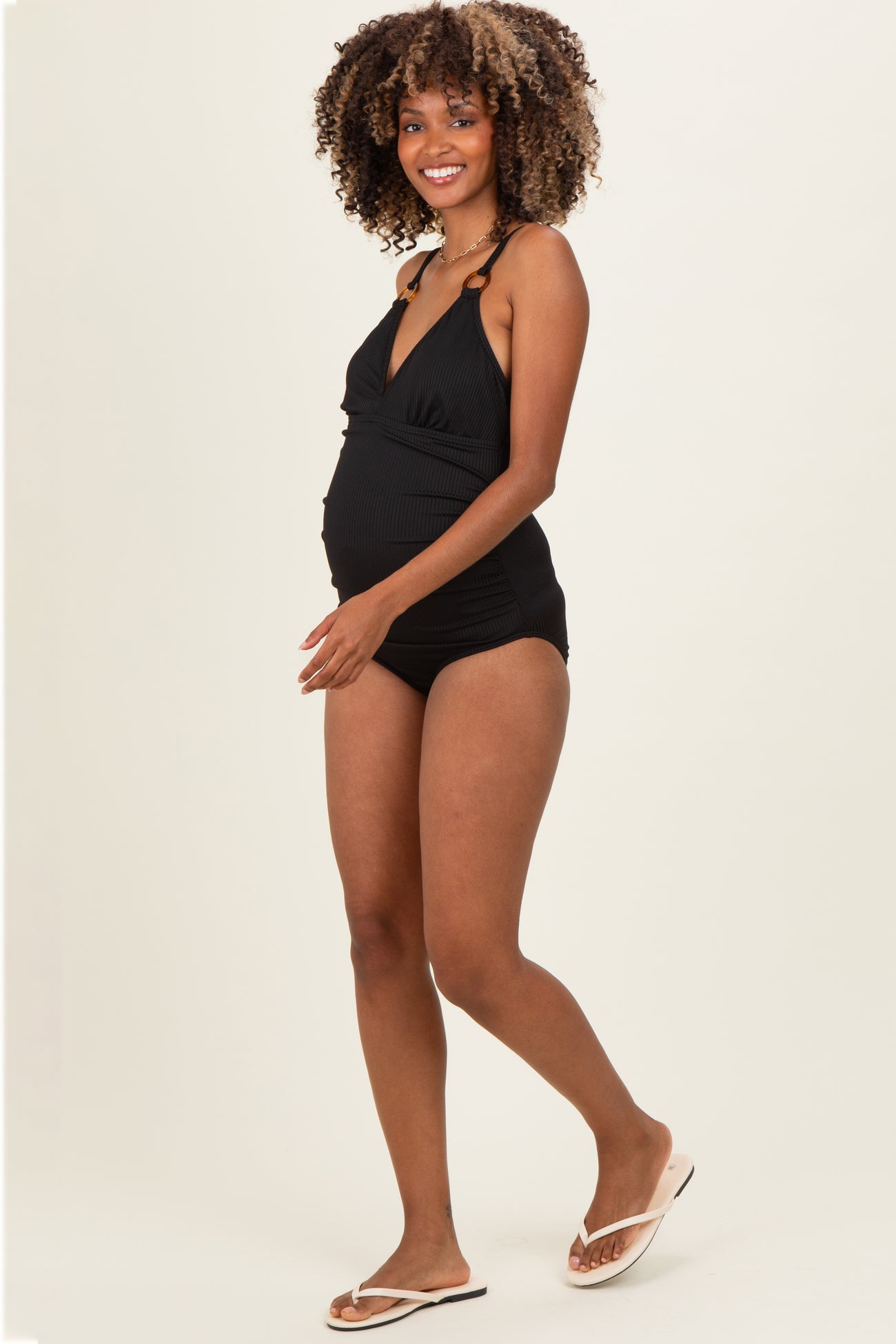 woman wearing a black maternity one-piece swimsuit with a deep v-neck and adjustable straps, showing her baby bump