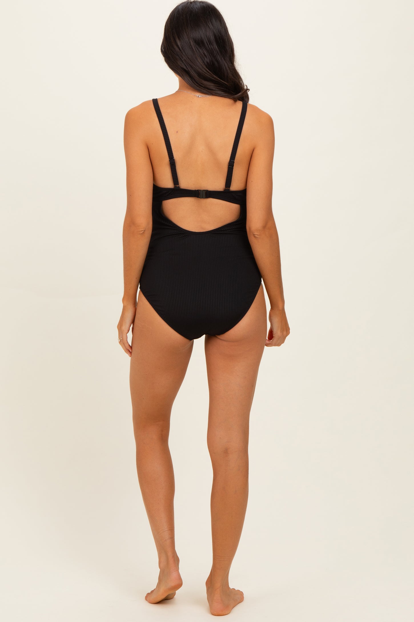 woman wearing a black ribbed one-piece swimsuit with a cut-out back detail