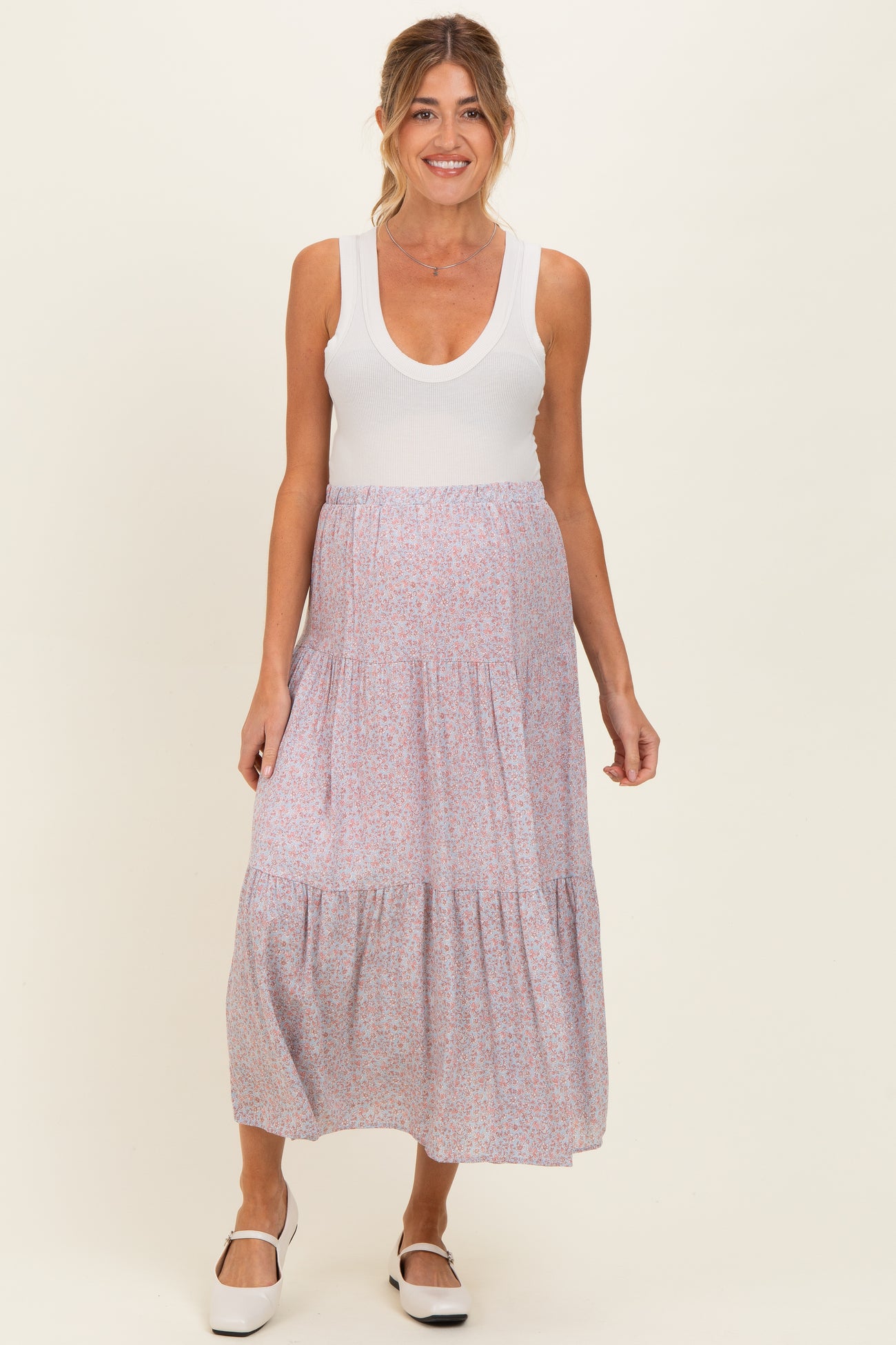 woman wearing a white ribbed maternity tank top and a floral maxi skirt, showing a baby bump