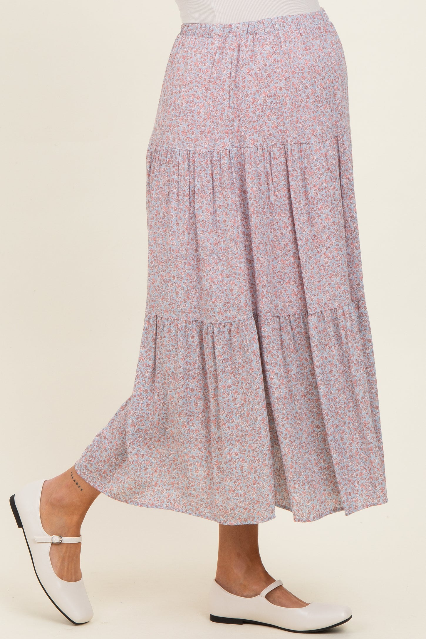 woman wearing a light pink floral maternity maxi skirt with tiered ruffles and a visible baby bump