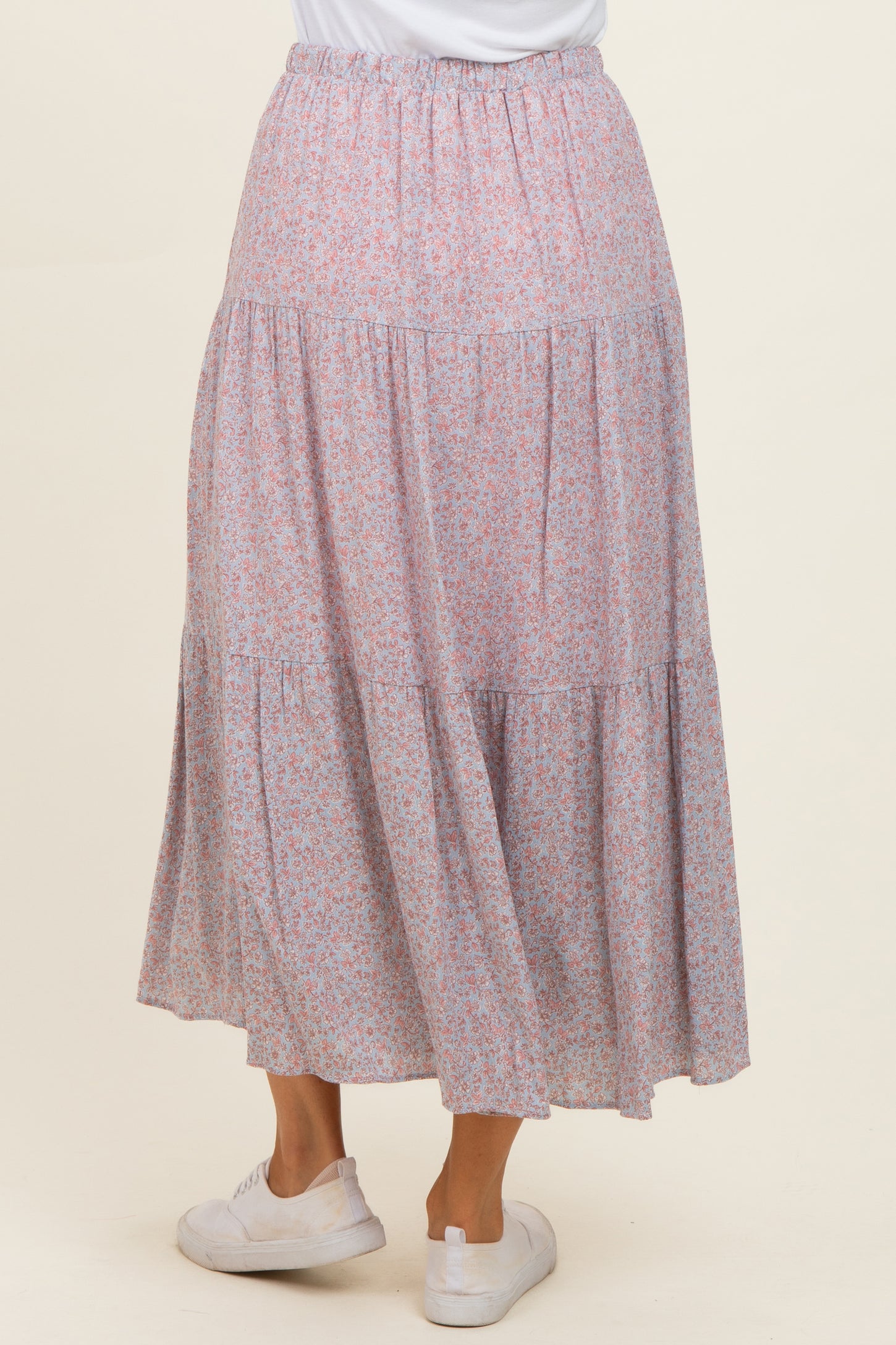 woman wearing a flowy pink floral tiered maxi skirt viewed from the back with an elastic waistband