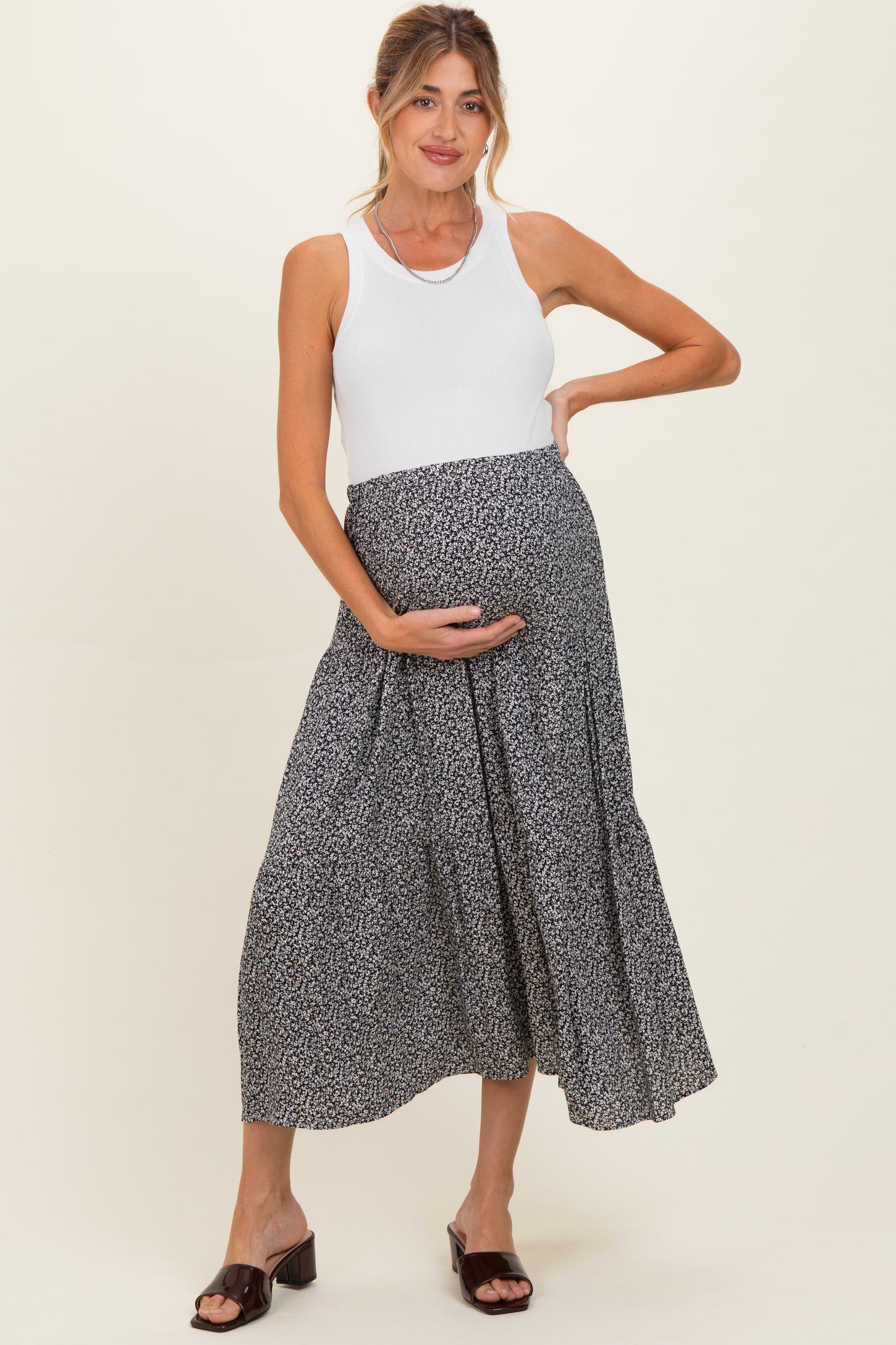 woman wearing a white tank top and a black floral maternity skirt, holding her baby bump
