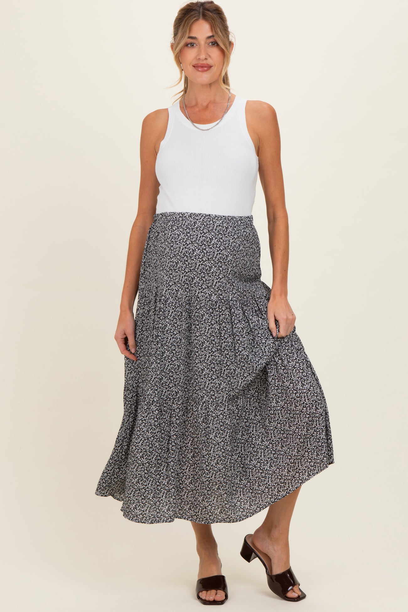 woman wearing a white tank top and a black and white floral print maternity skirt with ruffle detail
