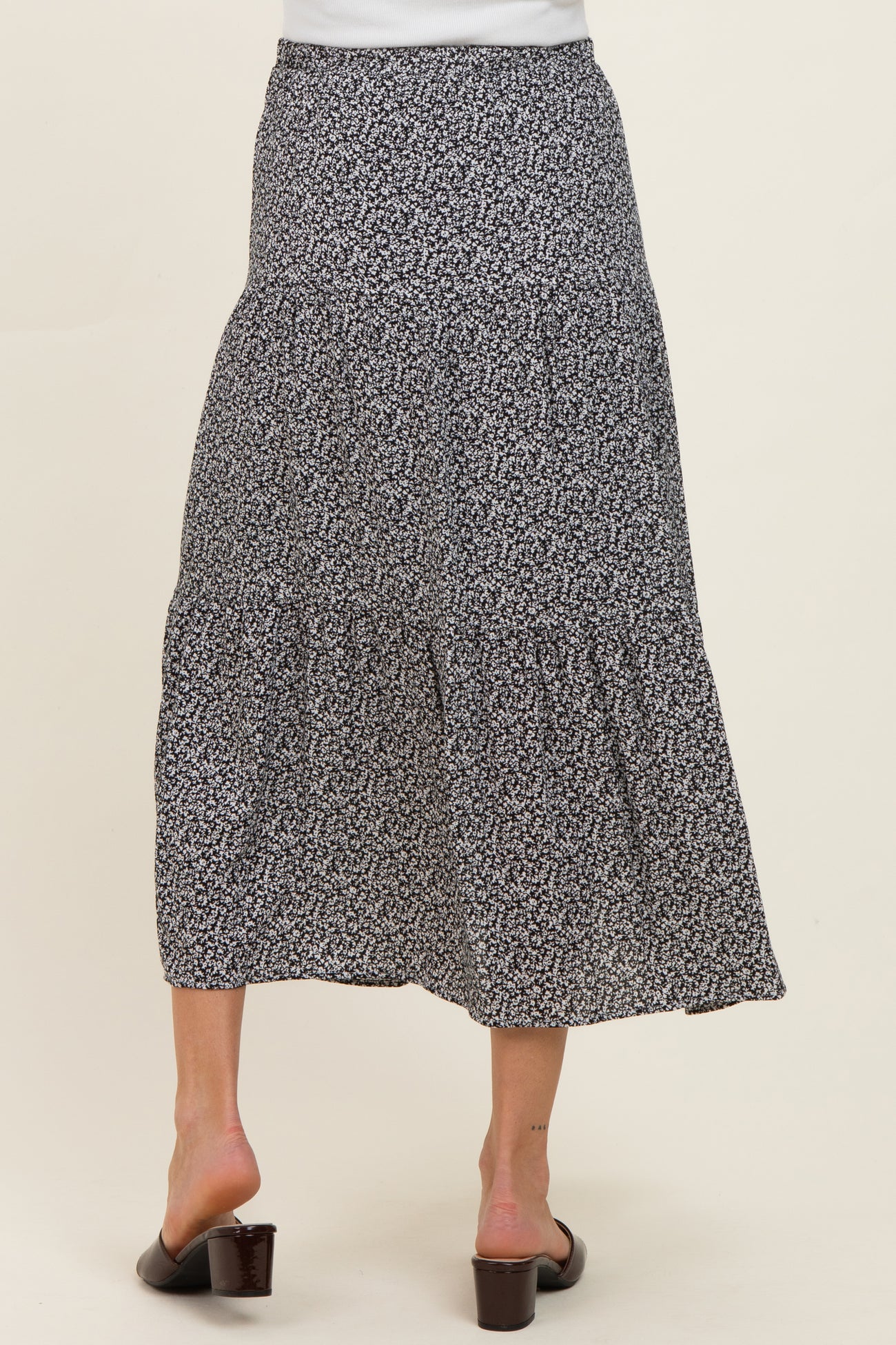 woman wearing a tiered black floral maternity skirt, shown from the back, with a flowy silhouette and below-the-knee length