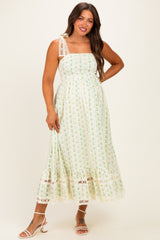 woman wearing a green and white floral print maternity dress with a square neckline and lace details, showing her baby bump