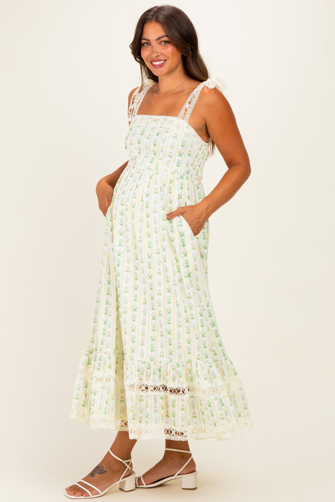 woman wearing a green and white floral maternity dress with lace details and pockets, showing her baby bump