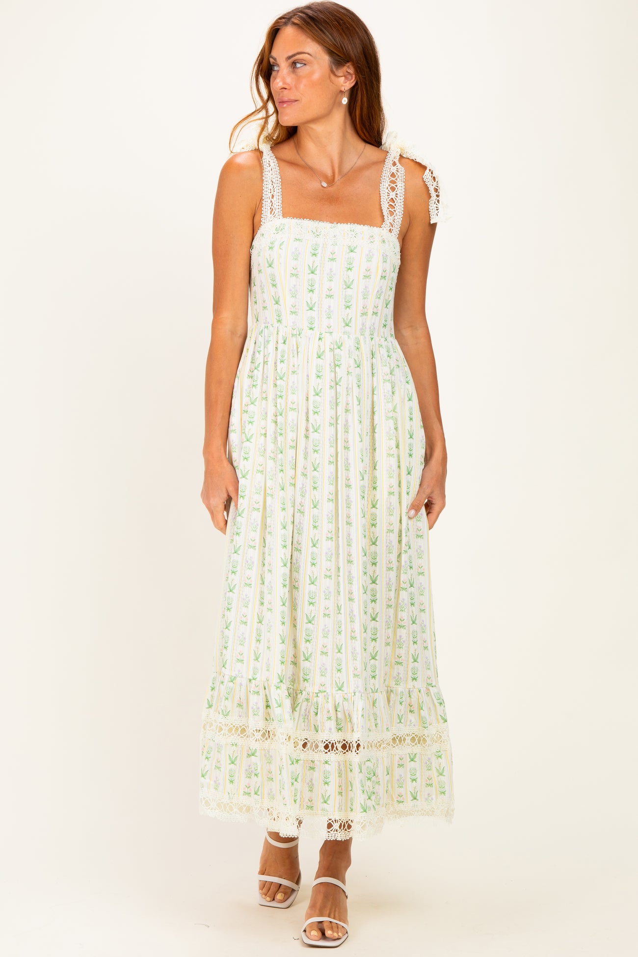 woman wearing a white and green floral maxi dress with lace trim and spaghetti straps