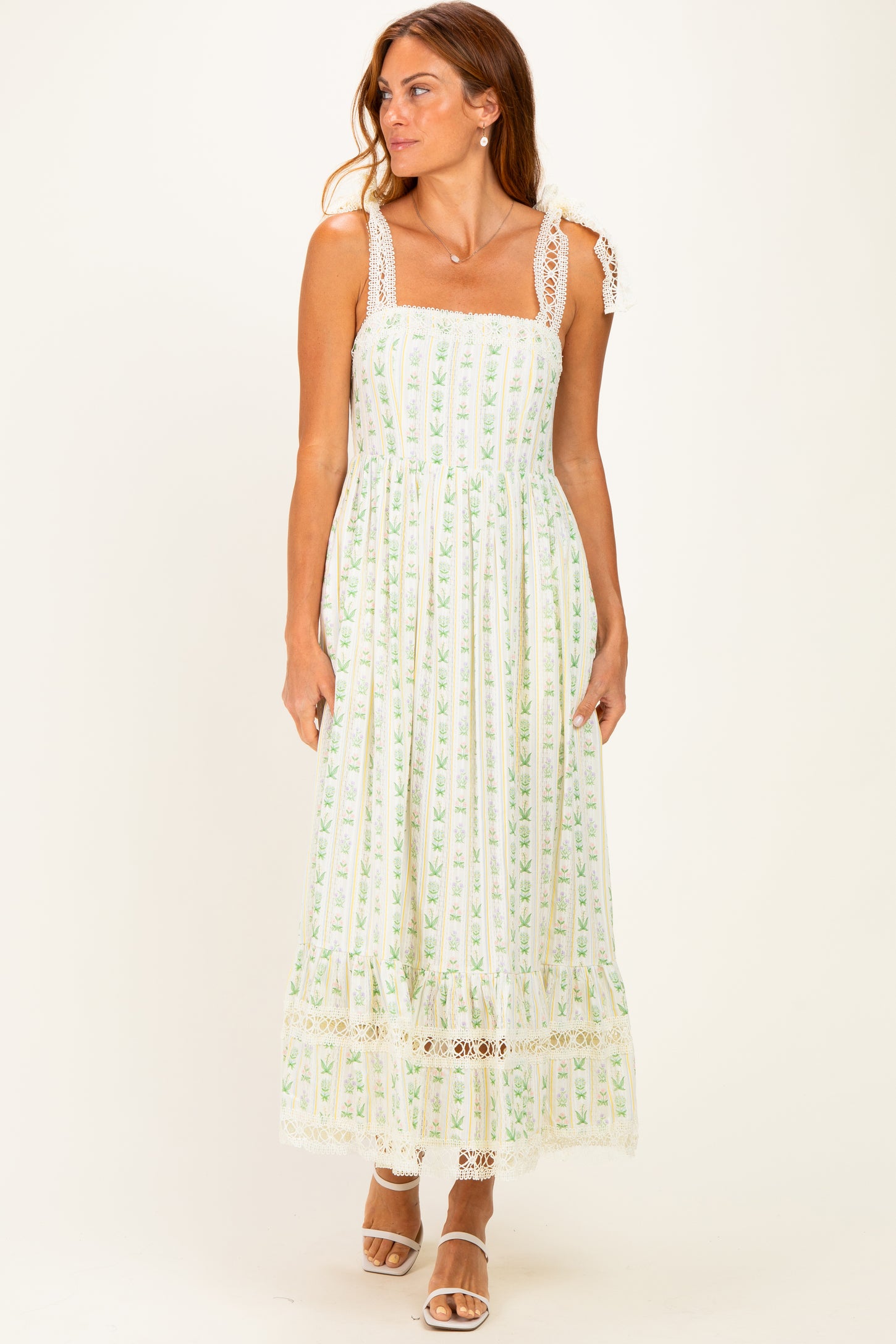 woman wearing a white and green floral maxi dress with lace trim and spaghetti straps